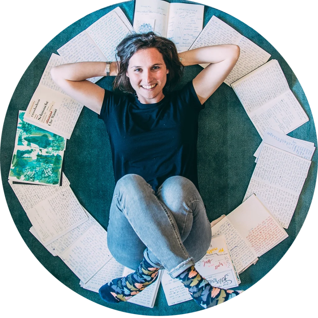 Irena liegt inmitten von Notizbüchern mit Texten die sie geschrieben hat in Kreisform um sie herum und sie lächelt zufrieden.