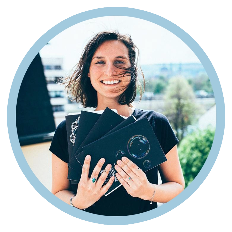 Irena steht auf einem Balkon ihr weht der Wind durch die Haare und sie lächelt in die Kamera und hält ihre voll geschriebenen Notizbücher wie einen Fächer vor sich.