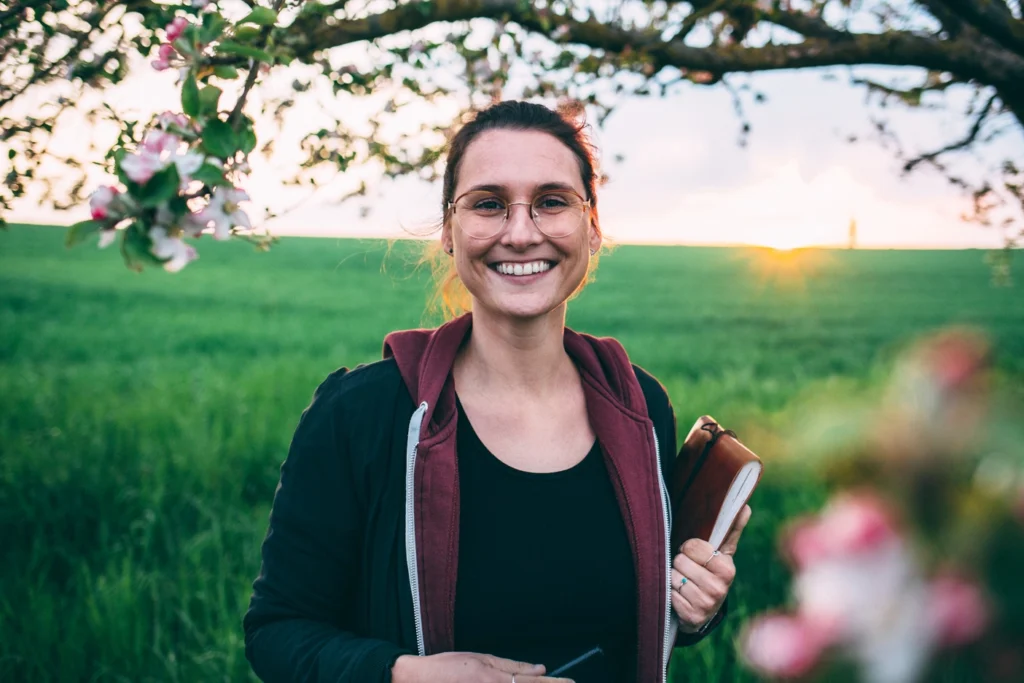 Irena steht mit ihrem Notizbuch vor einem Sonnenuntergang an einem grünen Feld unter einem blühenden Kirschbaum