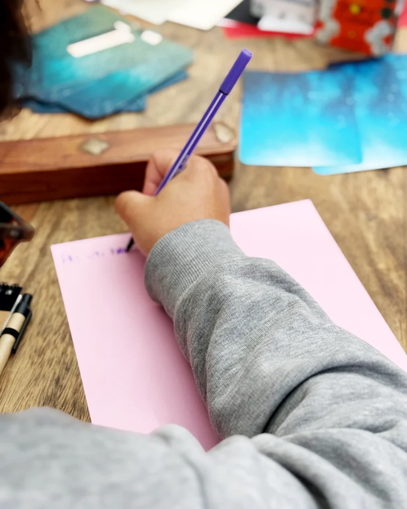 eine Hand schreibt auf ein buntes Blatt Papier einen Satzanfang mit einem Stift